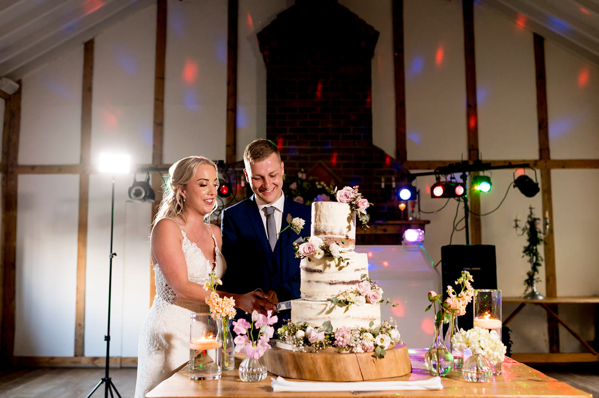 Couple cutting a floral semi-naked wedding cake